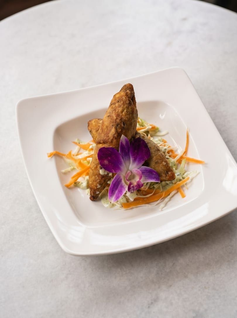 Crispy fried spring rolls on a bed of shredded cabbage and carrots, garnished with a purple orchid.