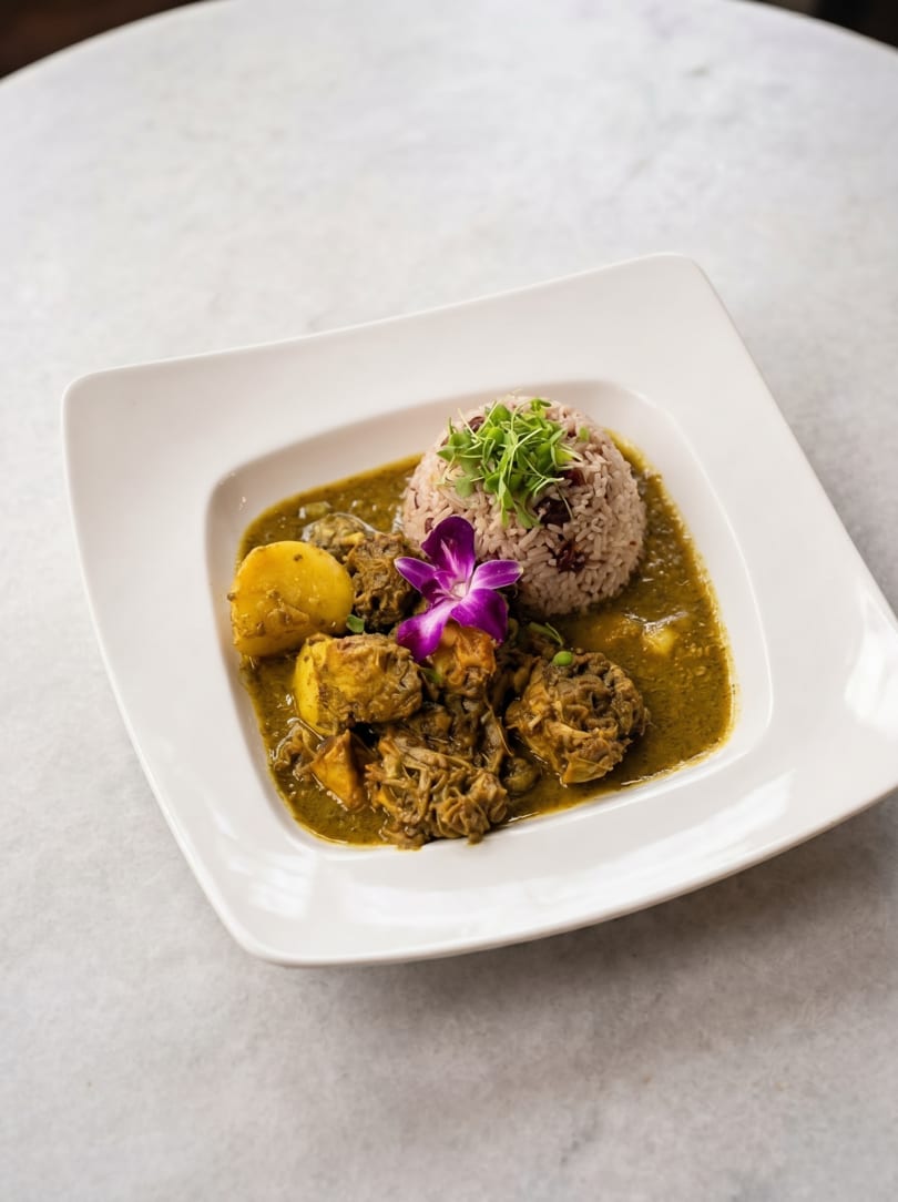 Curried chicken and potatoes in a green sauce, with rice and a purple orchid on a white plate.